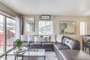 A living room with a leather sofa, a glass coffee table, and a view of a snowy landscape through large windows.