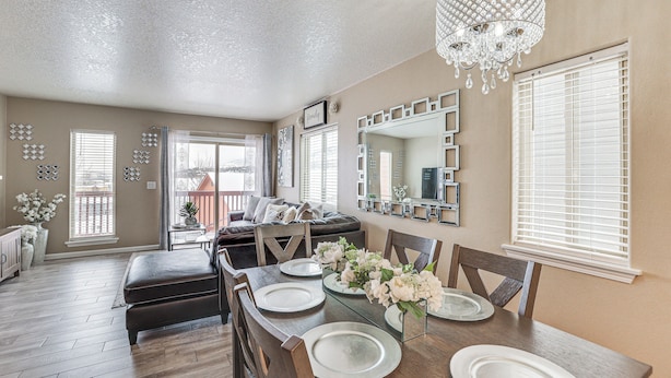 A dining area with a wooden table set for four, a chandelier, and a large mirror on the wall.