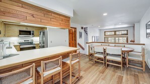 A modern kitchen with wooden cabinetry, a central island with seating, and a dining area with wooden chairs. - Walk to Chairlifts: Breck Condo w/ Private Patio (Breckenridge)