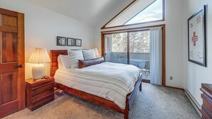 A bedroom with a large bed, wooden headboard, a nightstand with a lamp, and a window with a view of trees. - Walk to Chairlifts: Breck Condo w/ Private Patio (Breckenridge)