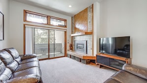 A modern living room with a leather sofa, a flat-screen TV, a fireplace, and a sliding glass door leading to a balcony. - Walk to Chairlifts: Breck Condo w/ Private Patio (Breckenridge)