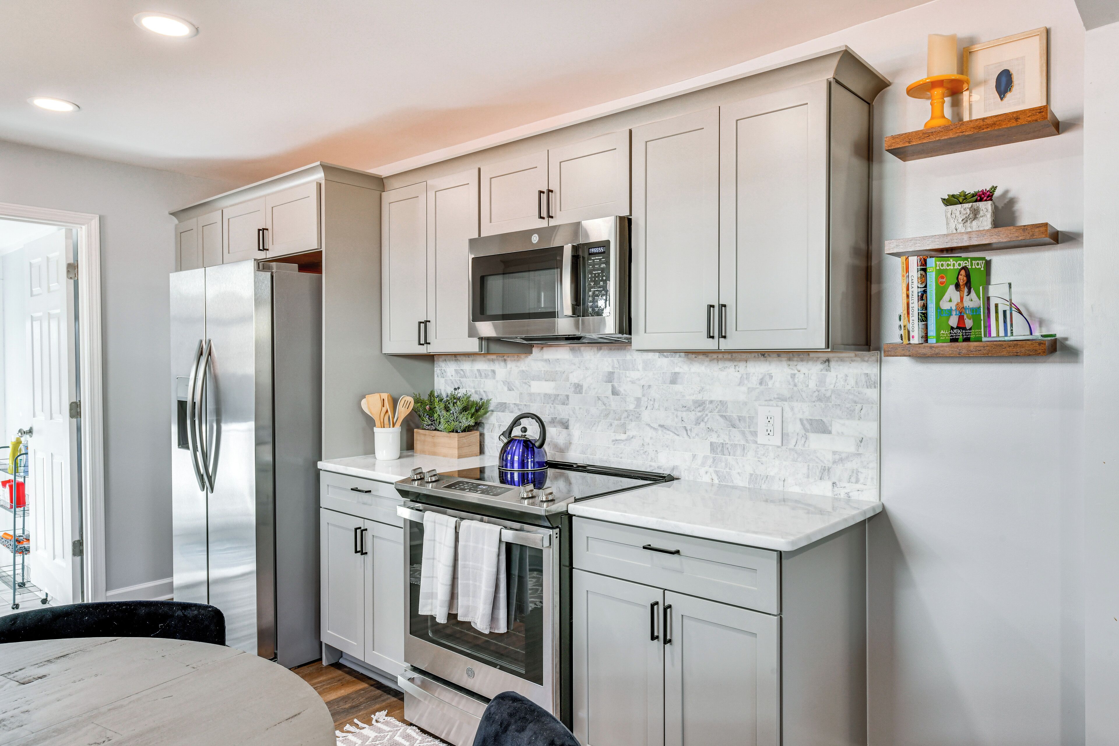 A modern kitchen with stainless steel appliances, white cabinetry, and a marble backsplash.