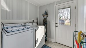 A laundry area with a Samsung washer and dryer, a drying rack, and a door with a view of the outside.