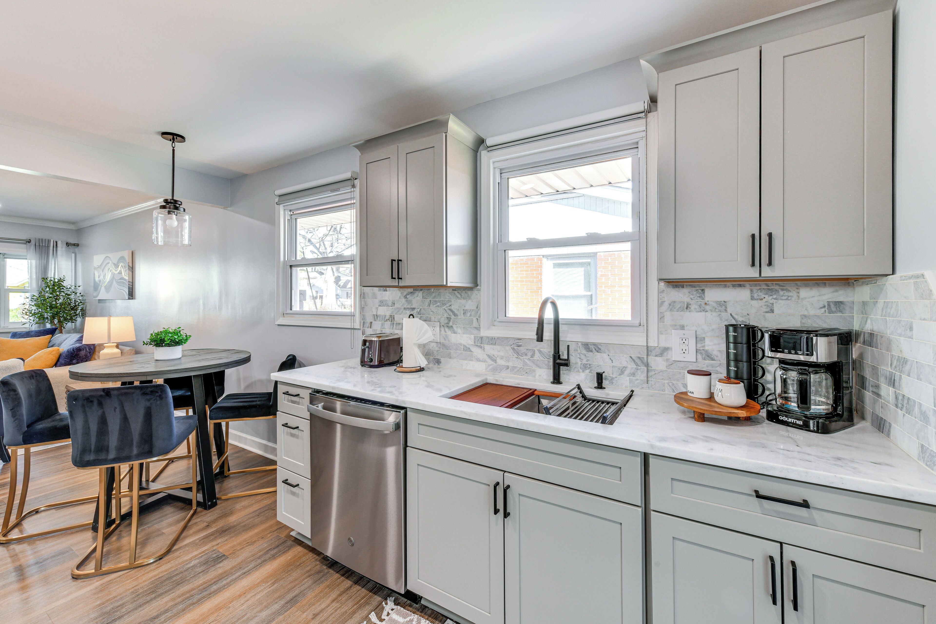 A modern kitchen with grey cabinets, a dishwasher, a coffee maker, and a dining area with a table and chairs.