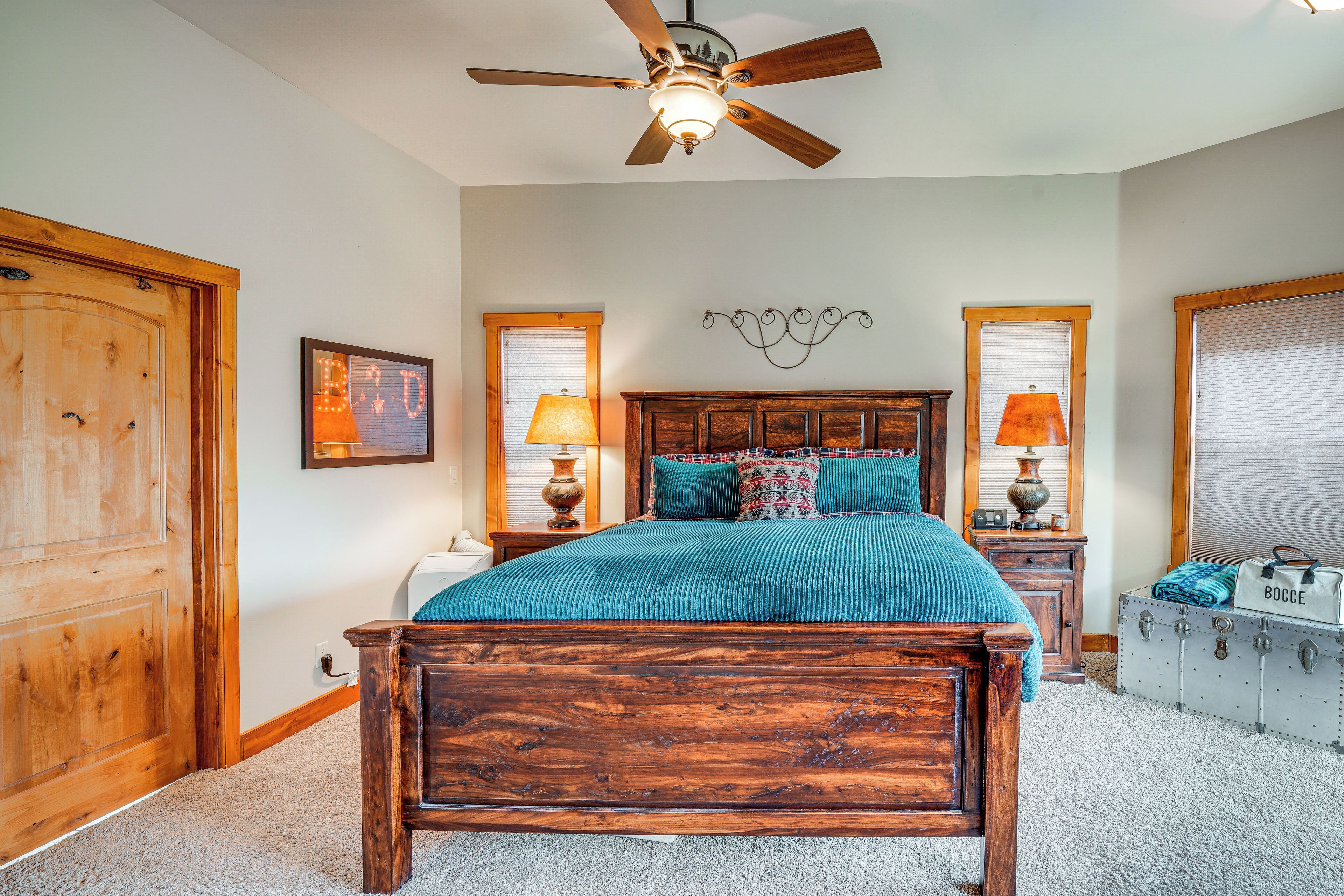 A bedroom with a wooden bed, two bedside tables with lamps, a ceiling fan, and a suitcase on the floor.