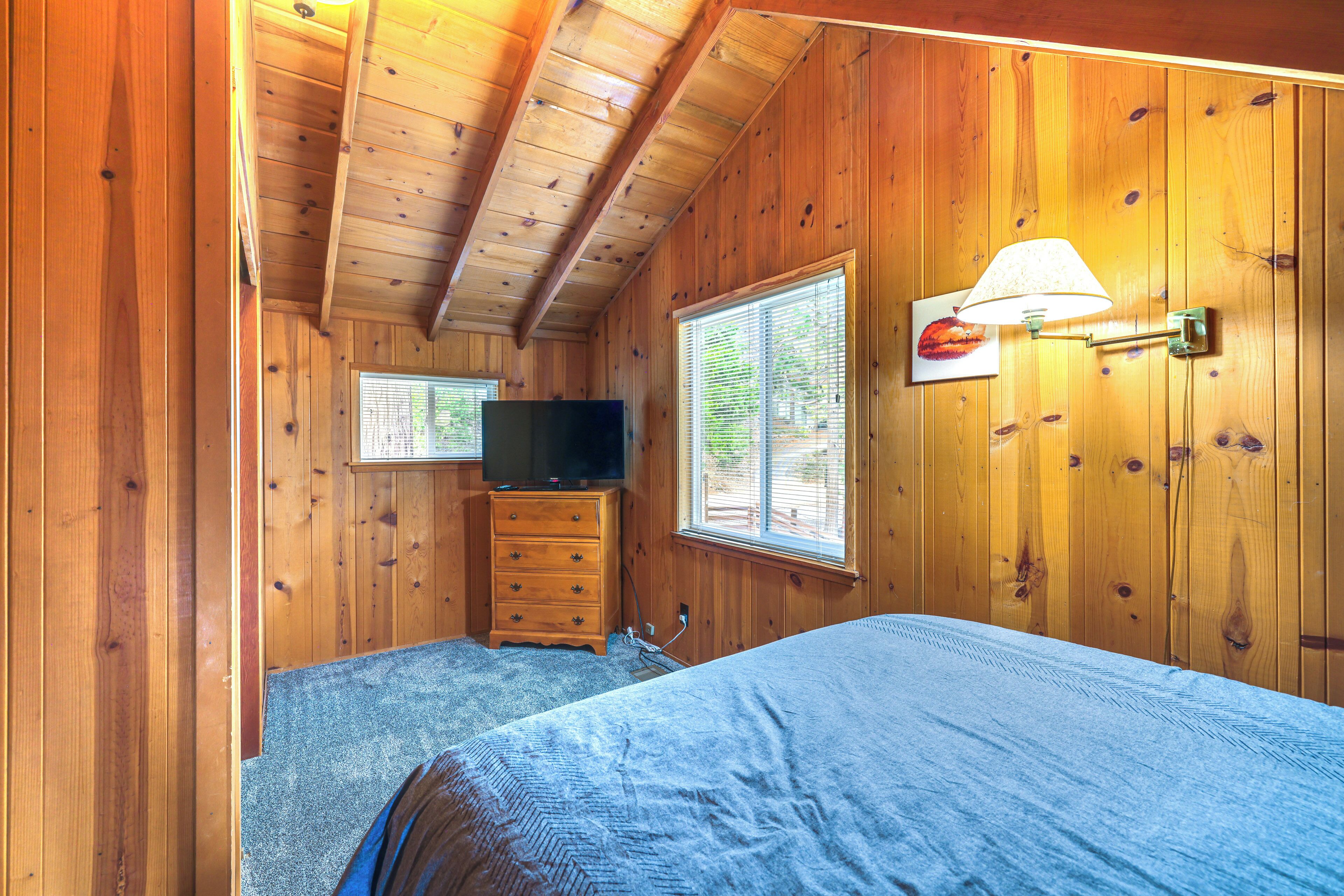 A wooden-paneled room with a bed, dresser, television, and a window with blinds.