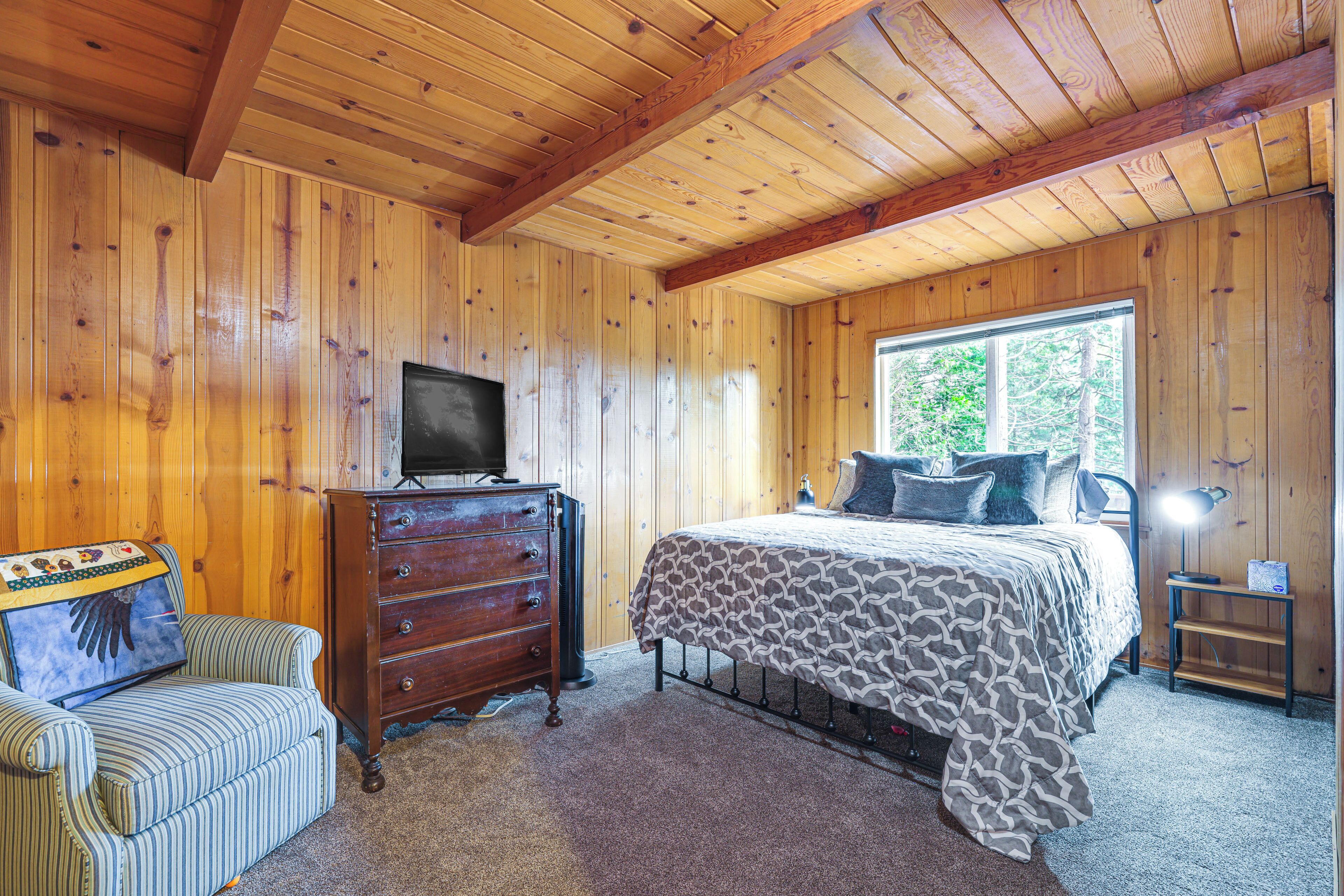 A wooden-paneled bedroom with a bed, dresser, and a television on a dresser.