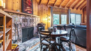 A cozy cabin interior with a stone fireplace, wooden ceiling, and a seating area with a cushioned bench.