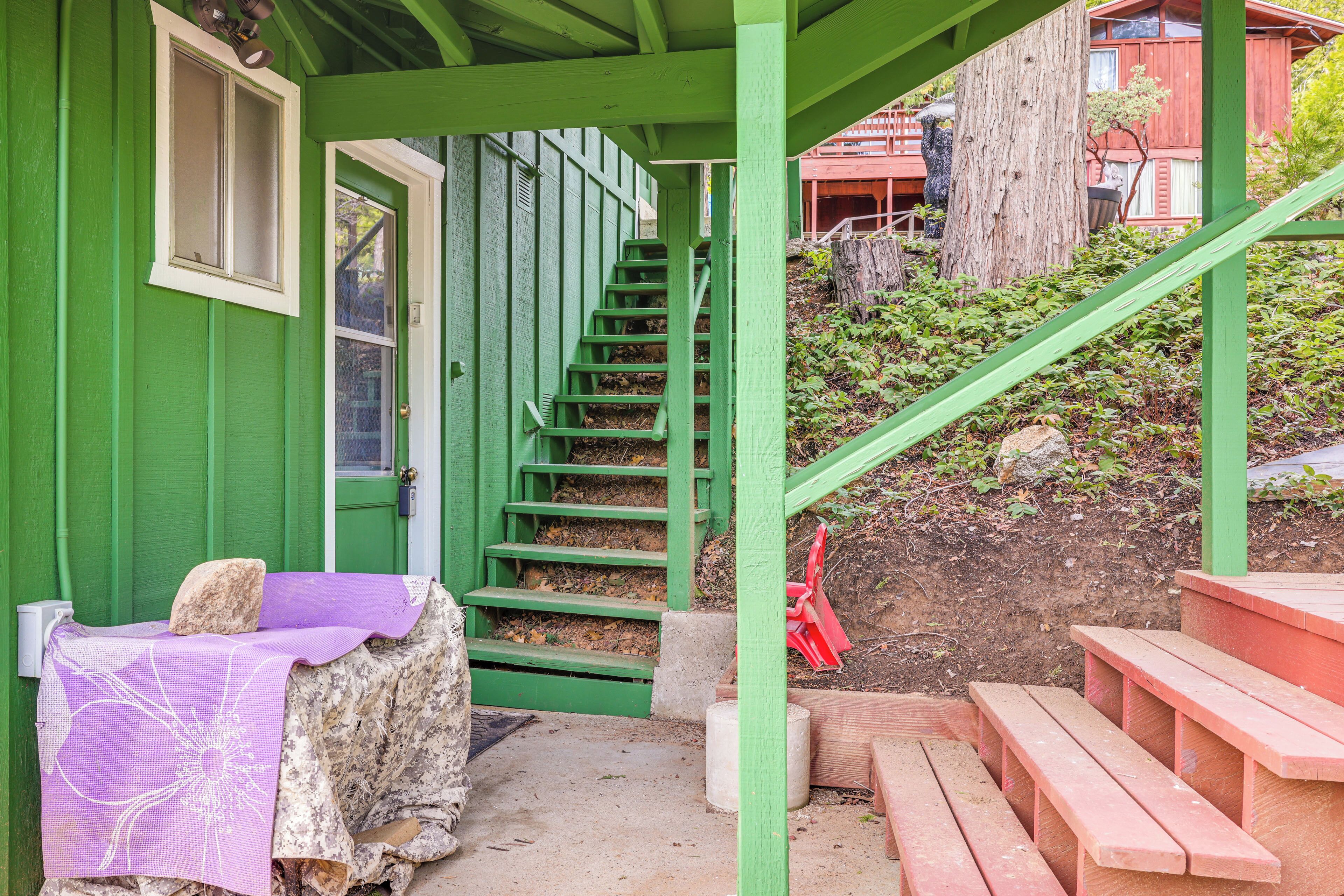 Una escalera verde que lleva a una puerta, con una mesa y un banco morados cerca.