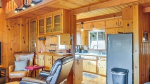 A cabin interior with wooden walls, a kitchenette, a seating area with a sofa and chairs, and a trash bin.