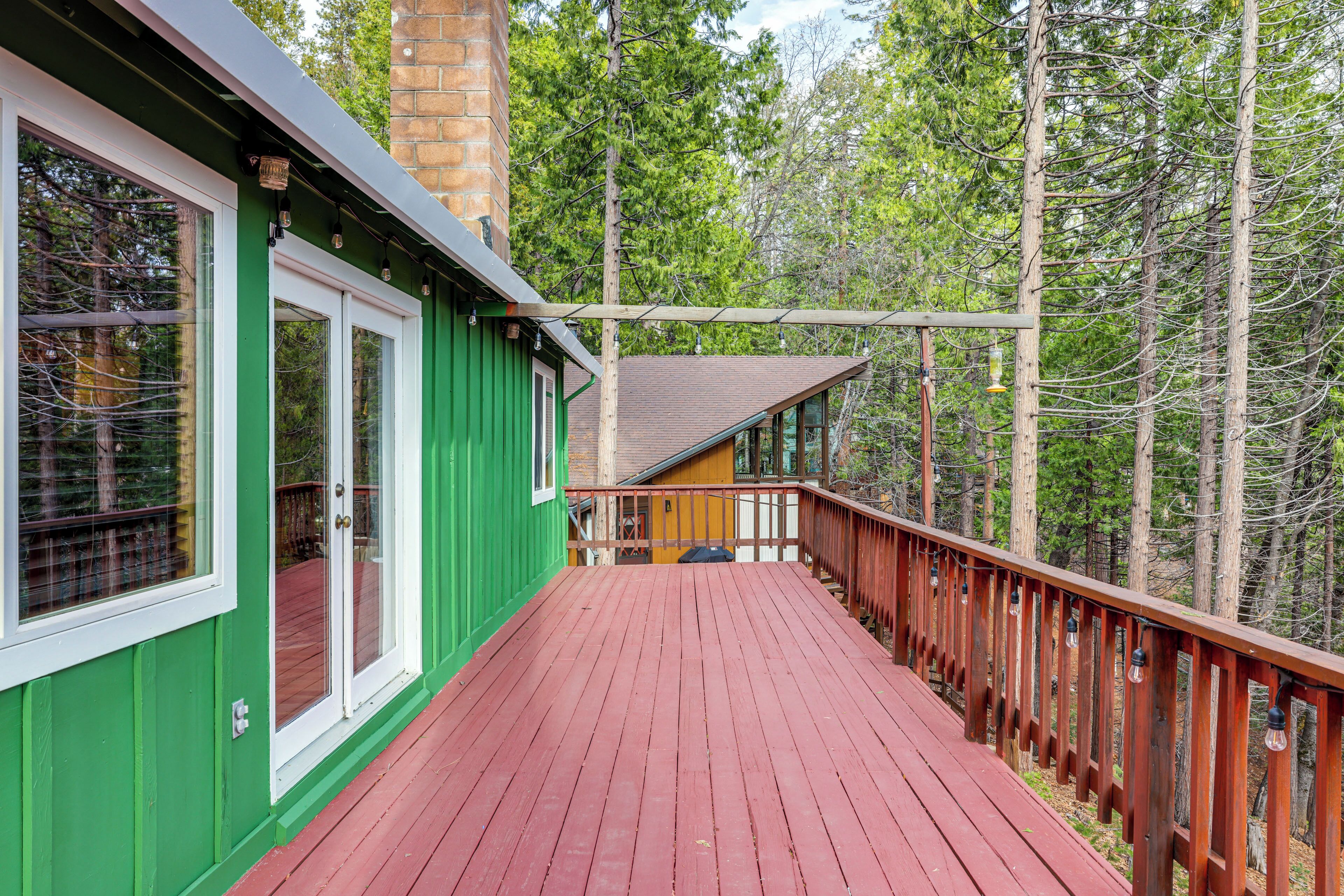 Una terraza de madera con baranda roja, paredes verdes y vista a un bosque.