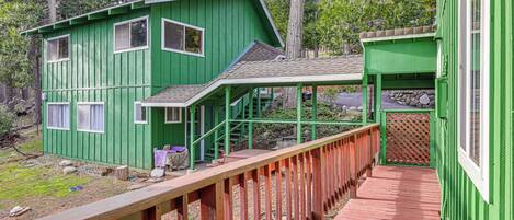 Une cabane en bois peinte en vert, avec une terrasse rouge, entourée d’arbres.