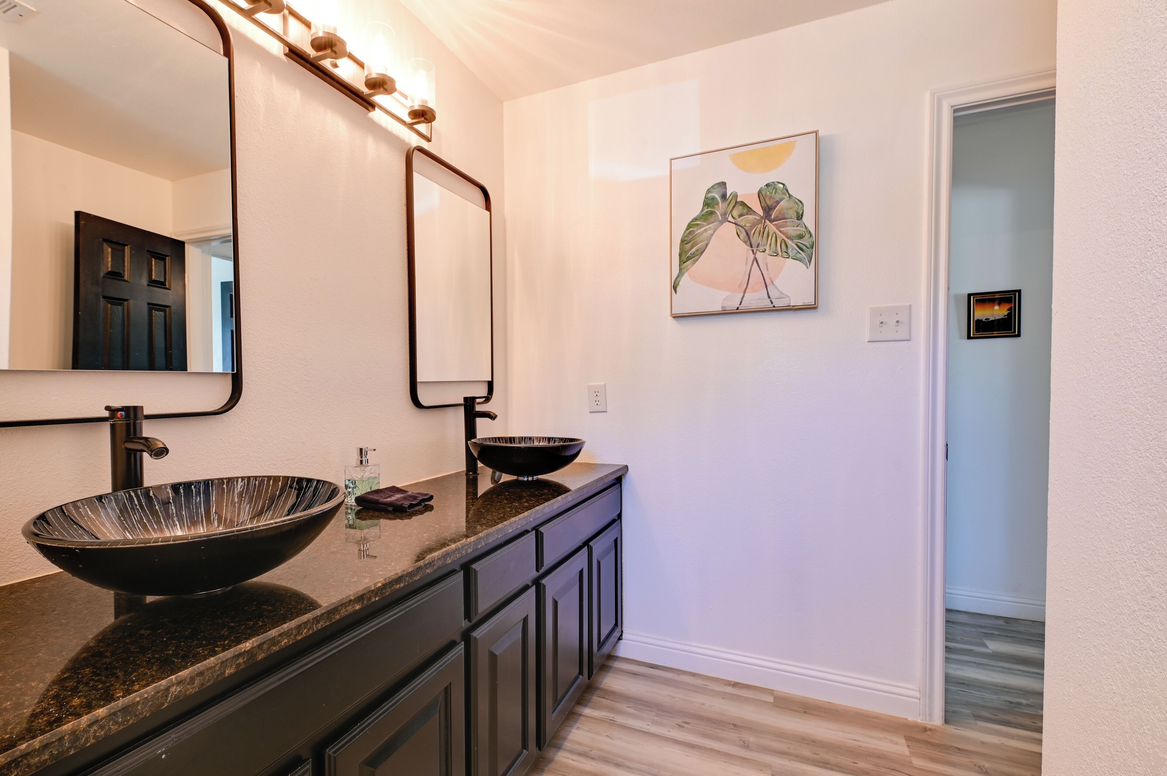 Une salle de bain avec un grand miroir, un lavabo noir sur pied et une plante décorative accrochée au mur.