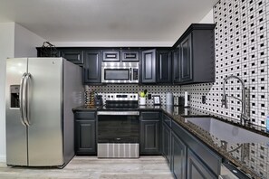 Une cuisine moderne avec des meubles de couleur sombre, des appareils électroménagers en acier inoxydable et un dosseret décoré.