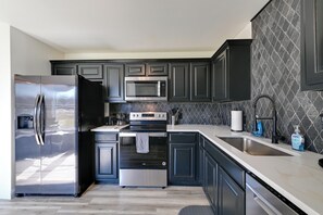 Una cocina moderna con armarios oscuros, electrodomésticos de acero inoxidable y un salpicadero con diseño de piedra.