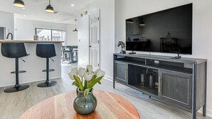 A modern kitchen with a dark wood cabinet, a large flat-screen TV, and two black bar stools. - 1 Mi to Beach: Cozy Grand Strand Townhome! (North Myrtle Beach)