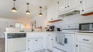 A kitchen with white cabinets, a dishwasher, an oven, a microwave, and pendant lights. - 1 Mi to Beach: Cozy Grand Strand Townhome! (North Myrtle Beach)