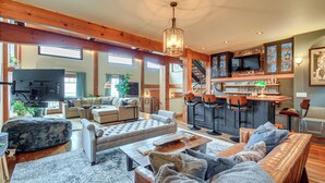 A spacious living area with a large sofa, a coffee table, and a fireplace. There is a kitchen area with a bar and stools, and a television mounted on the wall. - Luxury Vashon Vacation Rental w/ Beach Access! (Vashon Island)