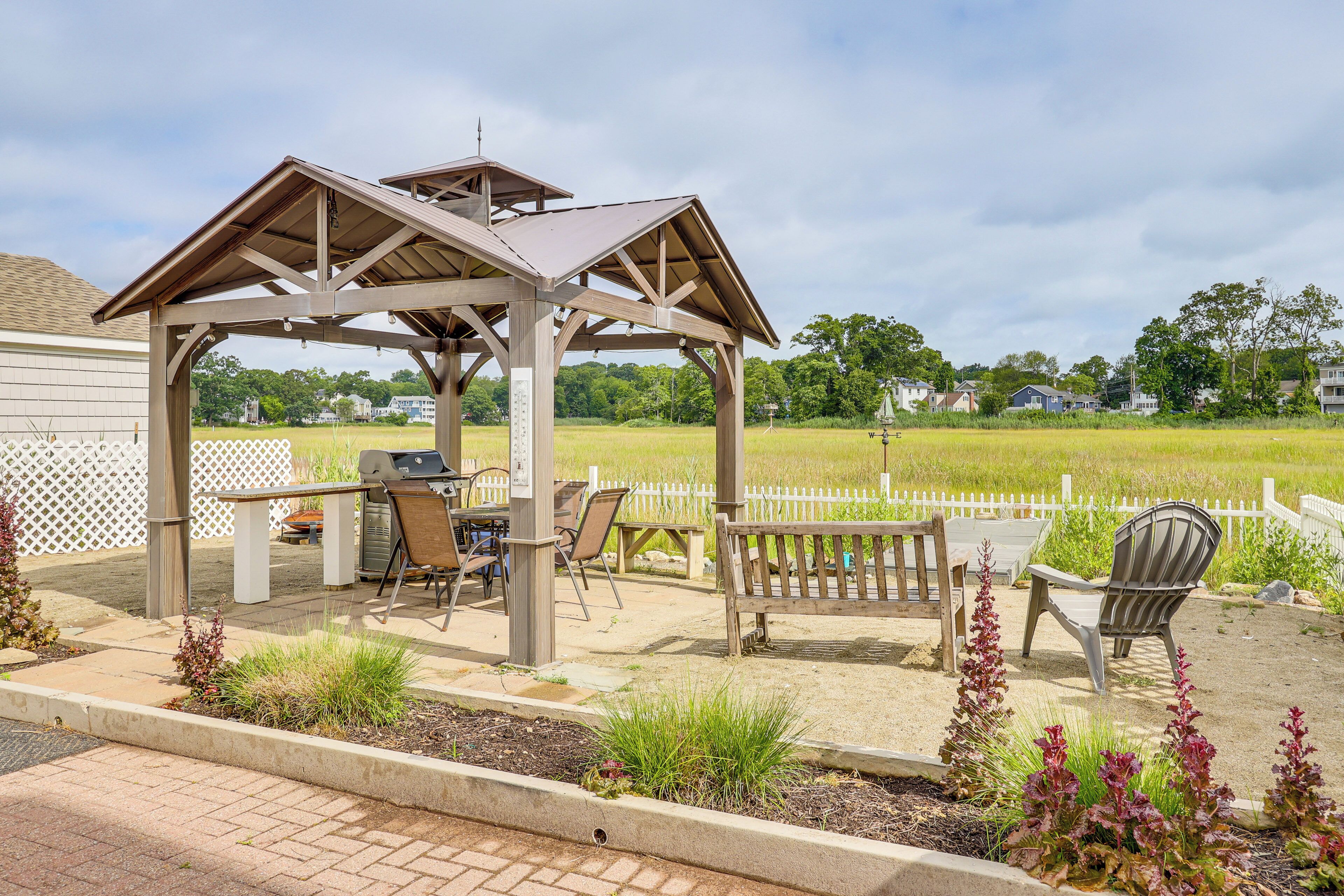 A gazebo with a picnic table and chairs, surrounded by a fenced yard with grass and plants.