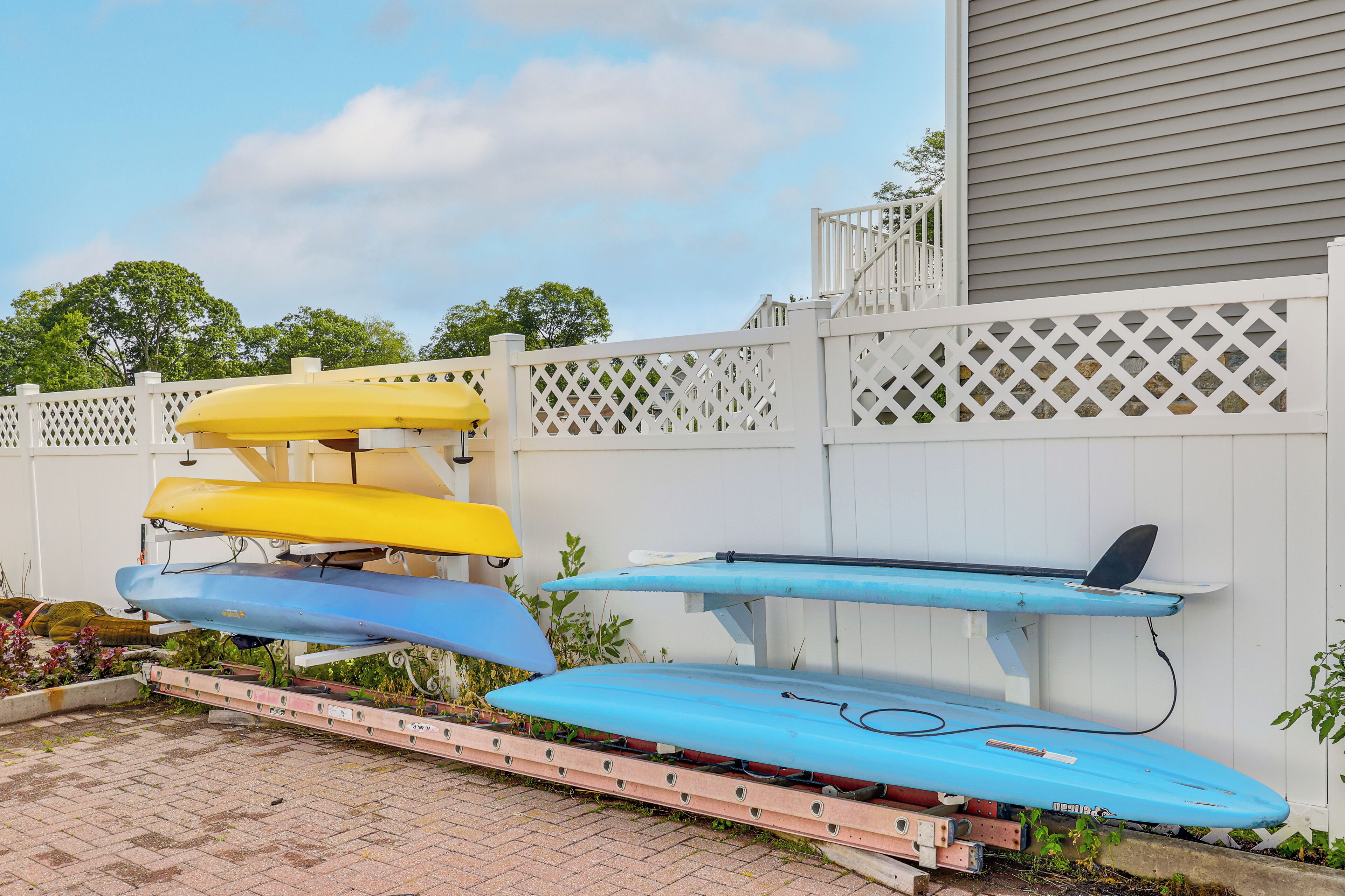 A white fence with a lattice design, a wooden deck, and a row of kayaks in yellow, blue, and light blue colors.