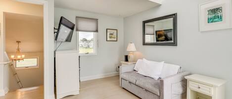 A modern living room with a grey sofa, a white side table, and a large window with blinds.