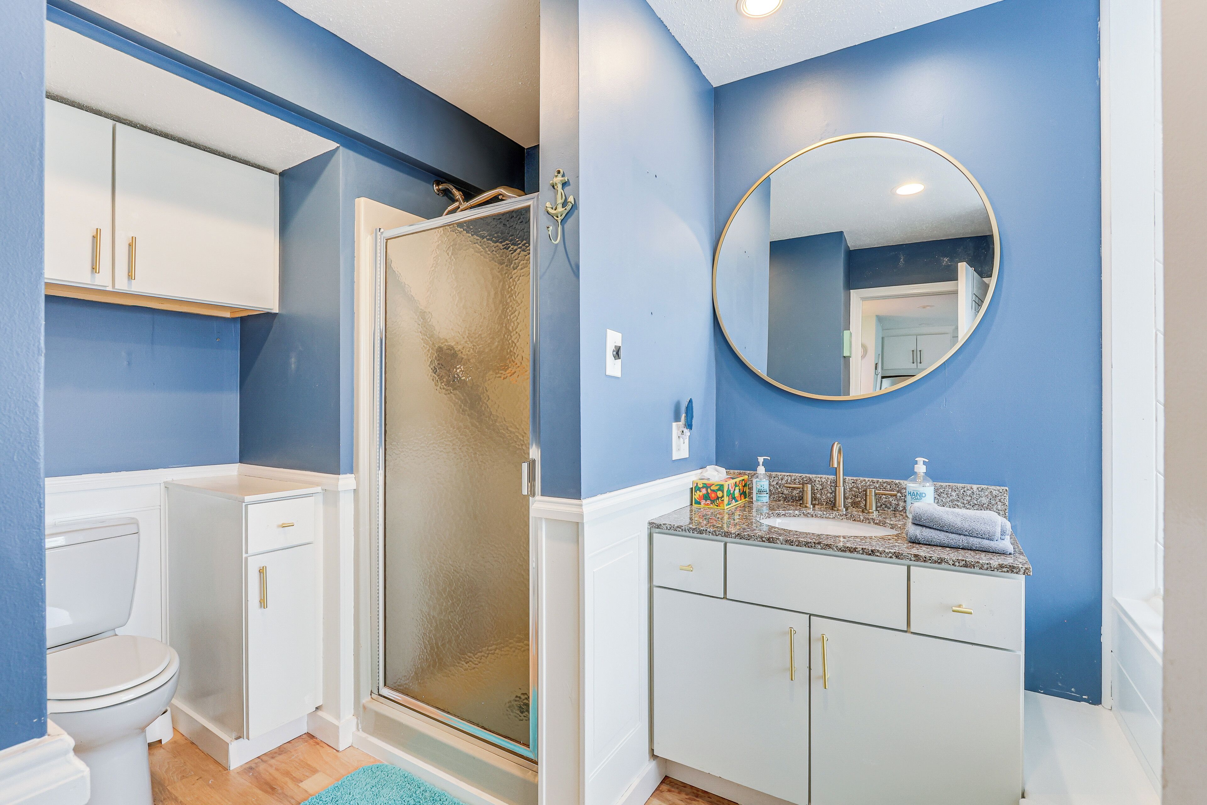 A bathroom with a toilet, a shower with a glass door, a sink with a mirror, and cabinets.
