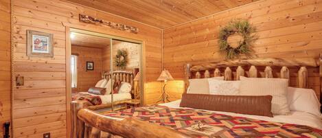 A wooden cabin bedroom with a bed, a nightstand, a lamp, and a mirror.