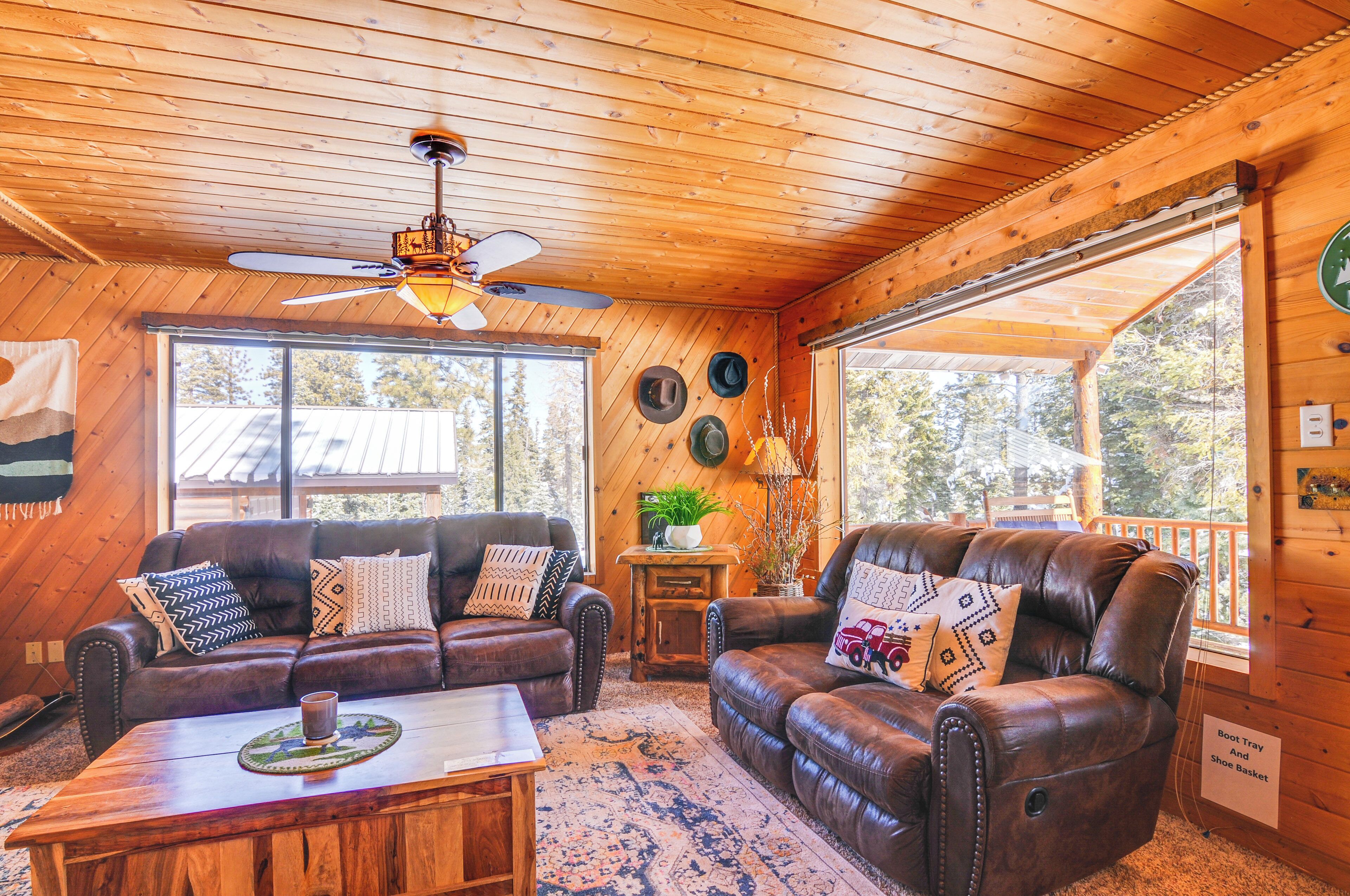 A cozy cabin interior with leather sofas, a wooden coffee table, and a ceiling fan.