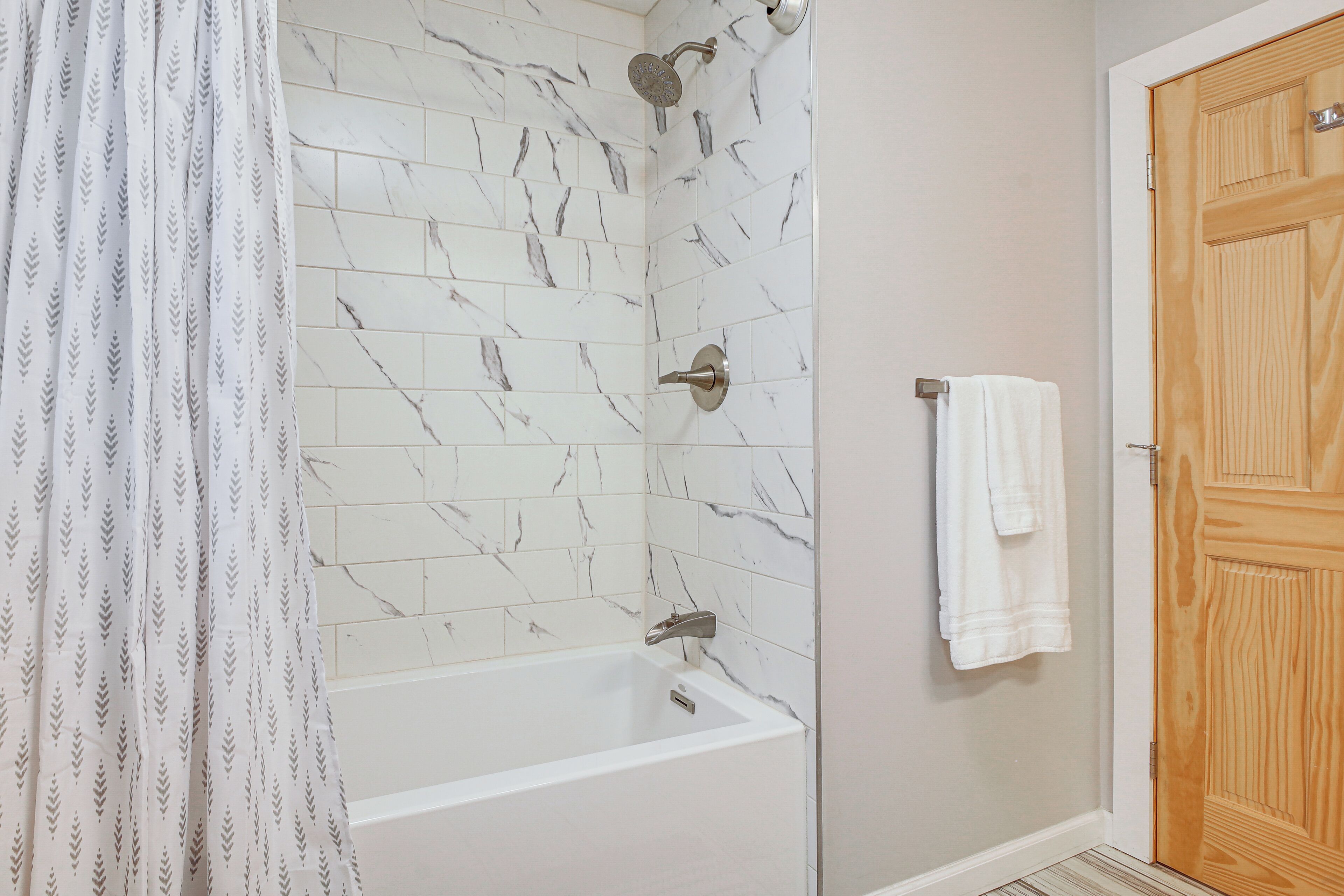 Une salle de bain avec une baignoire blanche, une pomme de douche et une porte en bois.