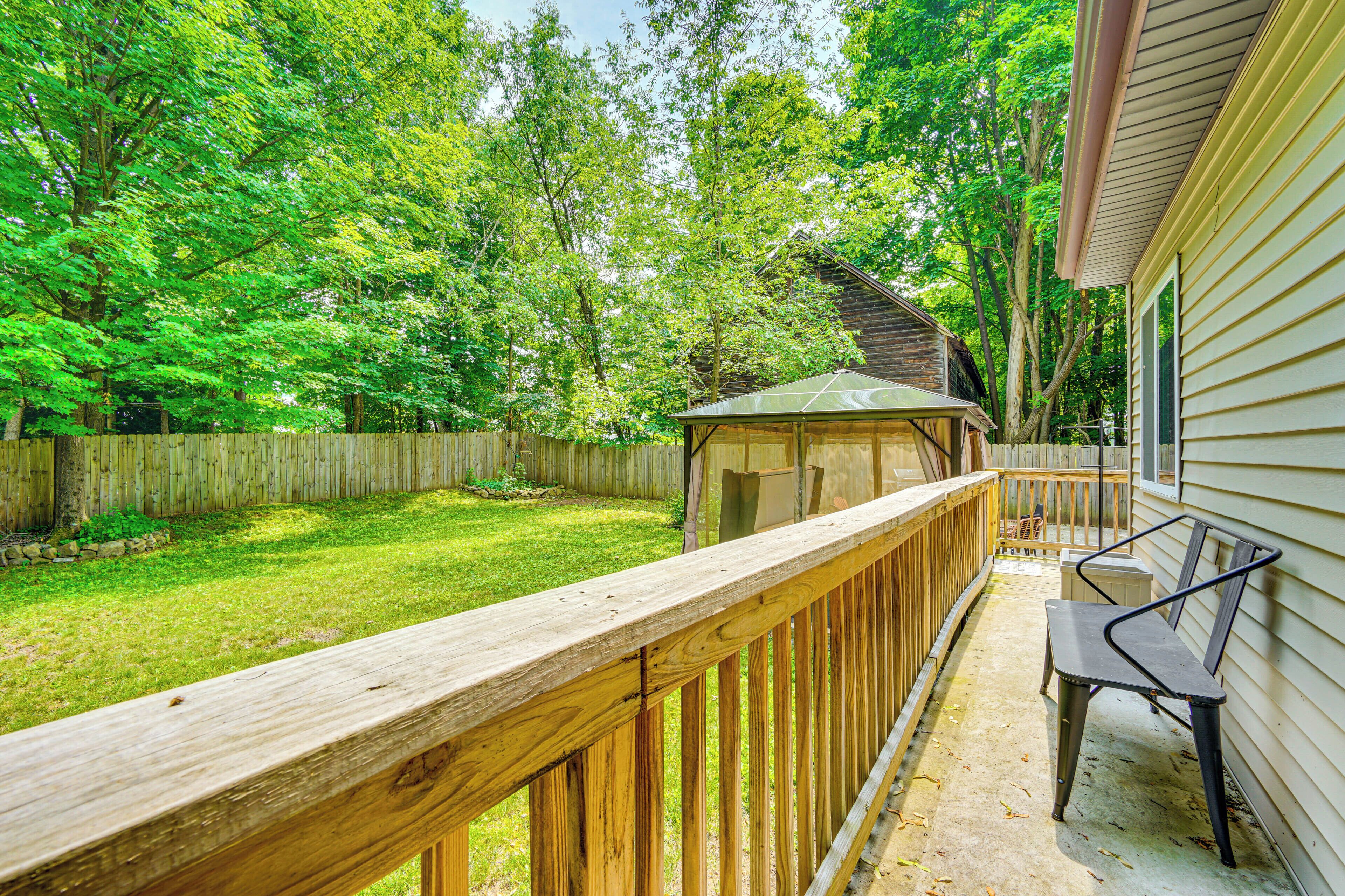 A wooden deck with a bench, a covered playhouse, and a fenced yard.