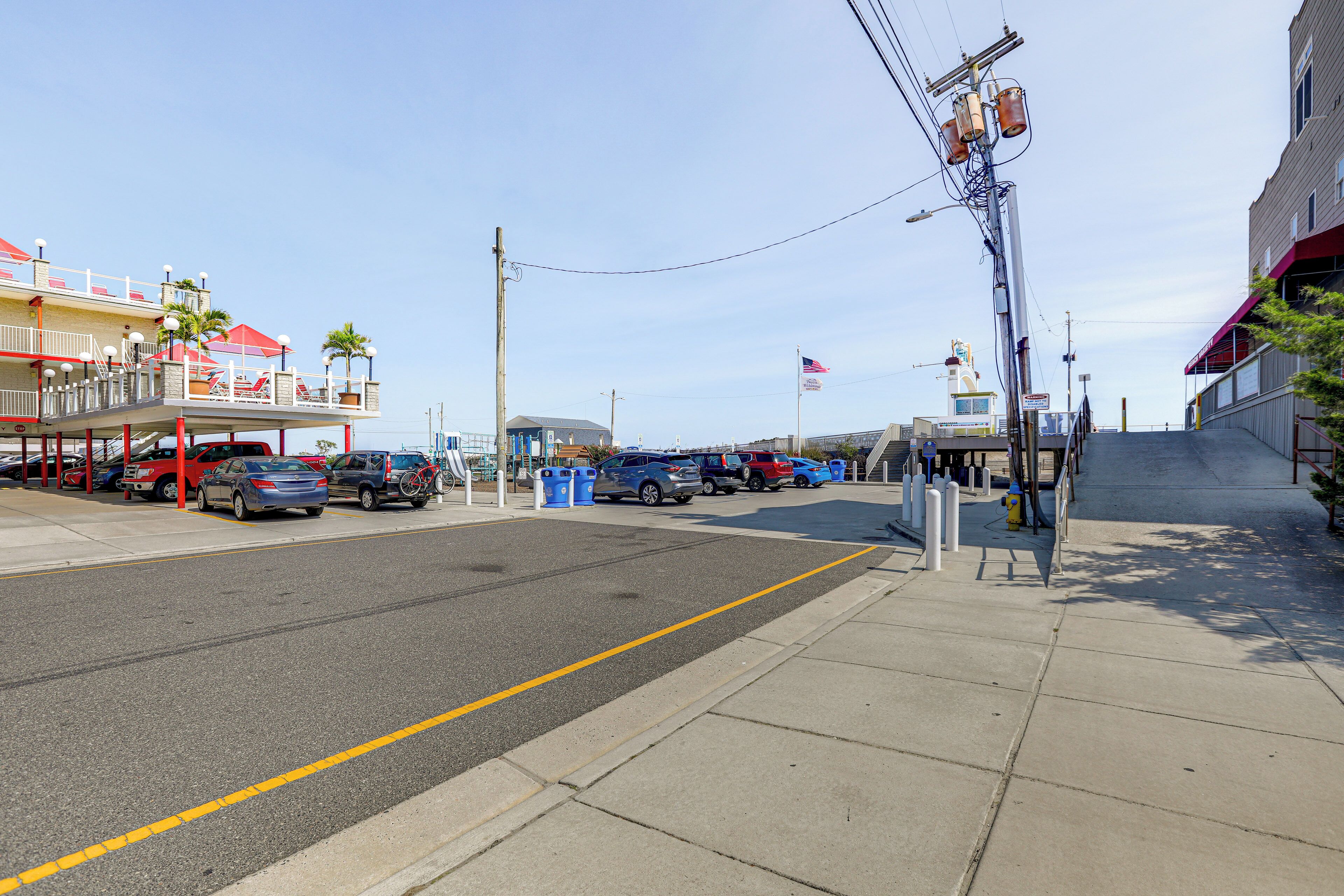 A street view with cars parked along the side, a sidewalk, and buildings with balconies and awnings.