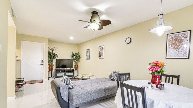 A modern living room with a sofa, a dining table with chairs, a ceiling fan, a TV, and a clock on the wall. - Houston Condo w/ Pool Access ~ 1 Mi to NRG Stadium (Houston)