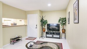 A living room with a flat-screen TV, a sofa, a coffee table, and two potted plants. - Houston Condo w/ Pool Access ~ 1 Mi to NRG Stadium (Houston)