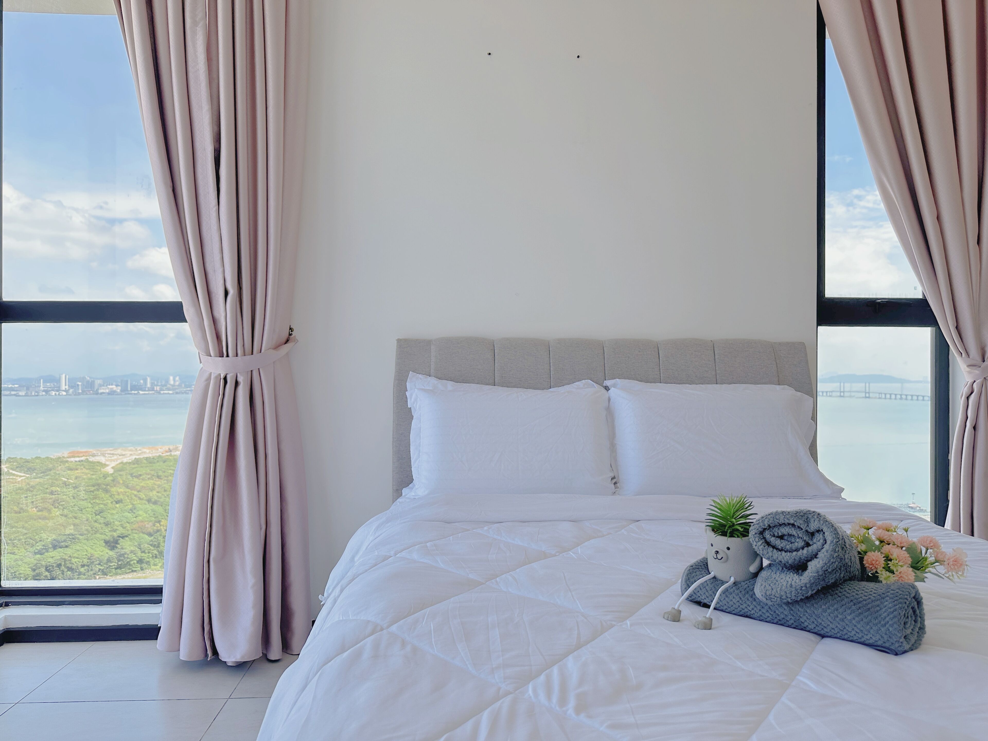 A bedroom with a large bed, a view of a cityscape and water, and a window with curtains.