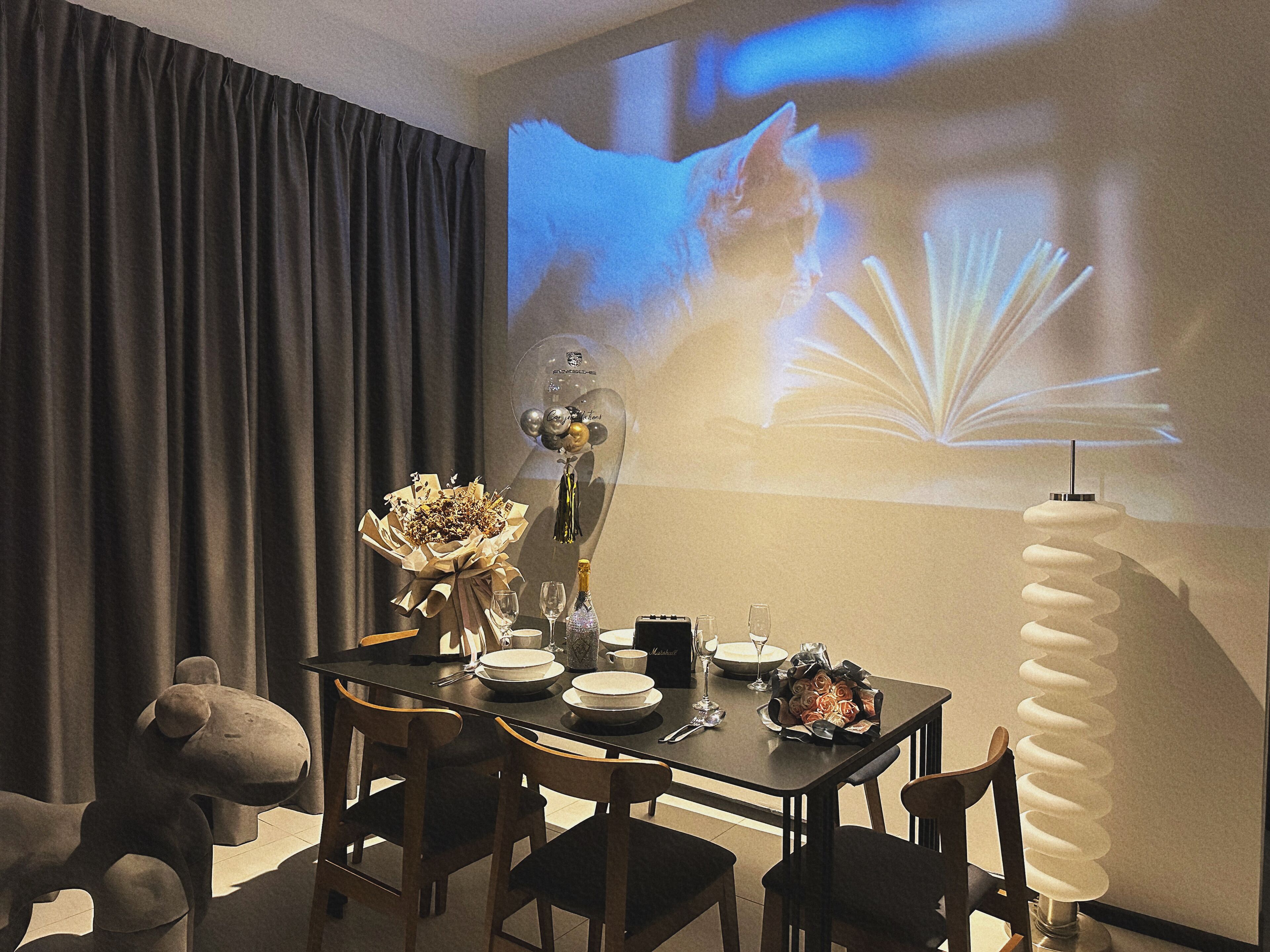 A dining area with a table set for two, a bouquet of flowers, and a projector screen displaying a cat.