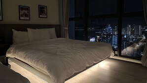 Une chambre d’hôtel avec un grand lit, une table de chevet et une vue sur le paysage urbain illuminé la nuit.
