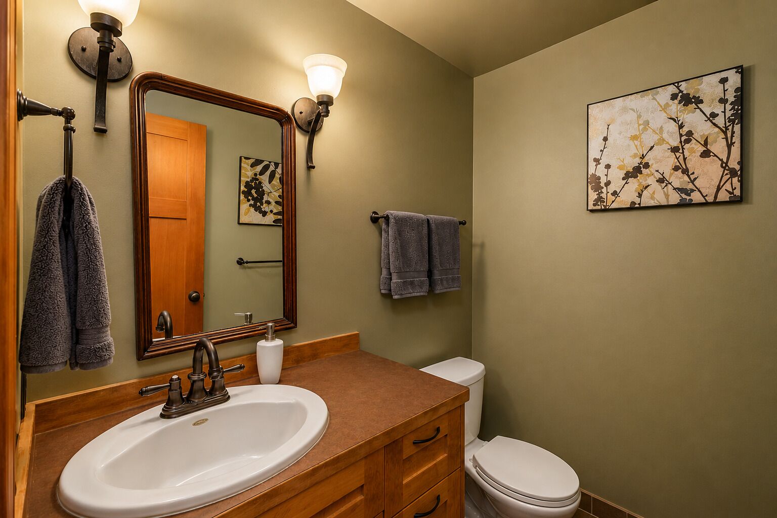 A bathroom with a sink, mirror, towel rack, toilet, and a wall-mounted artwork.
