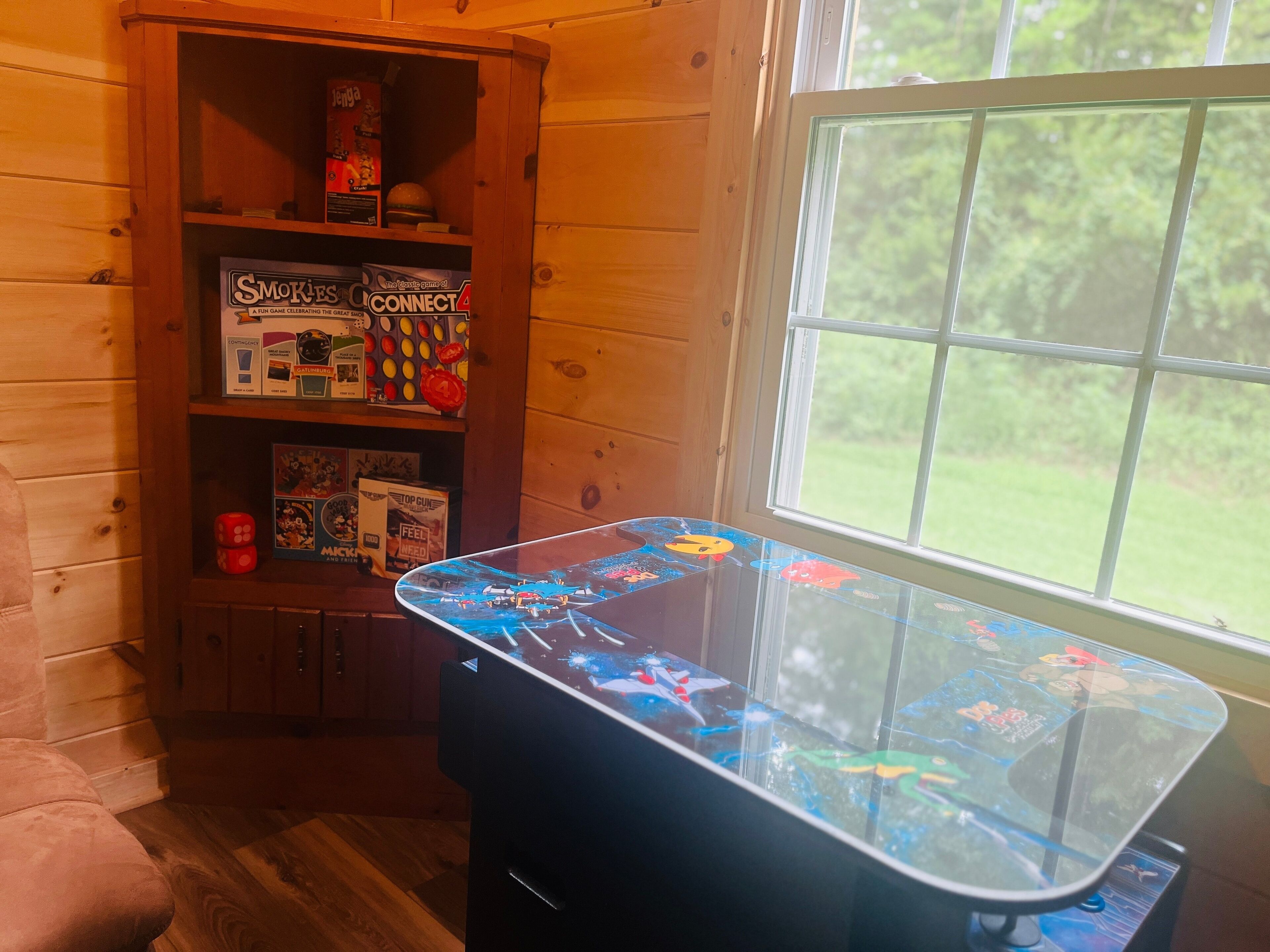 A room with a wooden interior, a glass-top table with a game, and a window with a view of greenery.