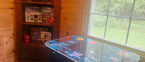 A room with a wooden interior, a glass-top table with a game, and a window with a view of greenery.