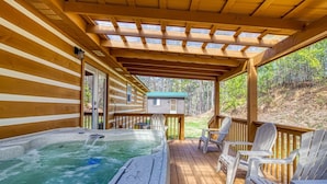 A wooden deck with a hot tub, chairs, and a covered area with a view of the surrounding forest. - Hilltop Hideaway 3 Bedroom Cabin by RedAwning (Sevierville)