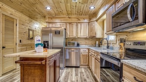 A modern kitchen with wooden cabinetry, stainless steel appliances, and a granite countertop. - Hilltop Hideaway 3 Bedroom Cabin by RedAwning (Sevierville)