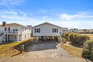 A two-story house with a covered patio, a staircase, and a small outdoor seating area. - Dunebug Cottage / 319 Sandpiper Lane 3 Bedroom Home by RedAwning (Supply)