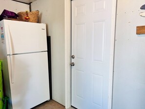 A white refrigerator, a closed door, and a corner with a white wall. - Dunebug Cottage / 319 Sandpiper Lane 3 Bedroom Home by RedAwning (Supply)