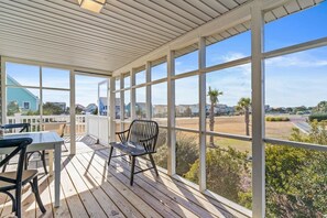 Un espace extérieur abrité, doté d’une table et de chaises, de grandes fenêtres et offrant une vue sur un quartier résidentiel.