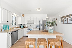 A modern kitchen with white cabinetry, a central island with stools, stainless steel appliances, and a 'Welcome' sign on the wall.