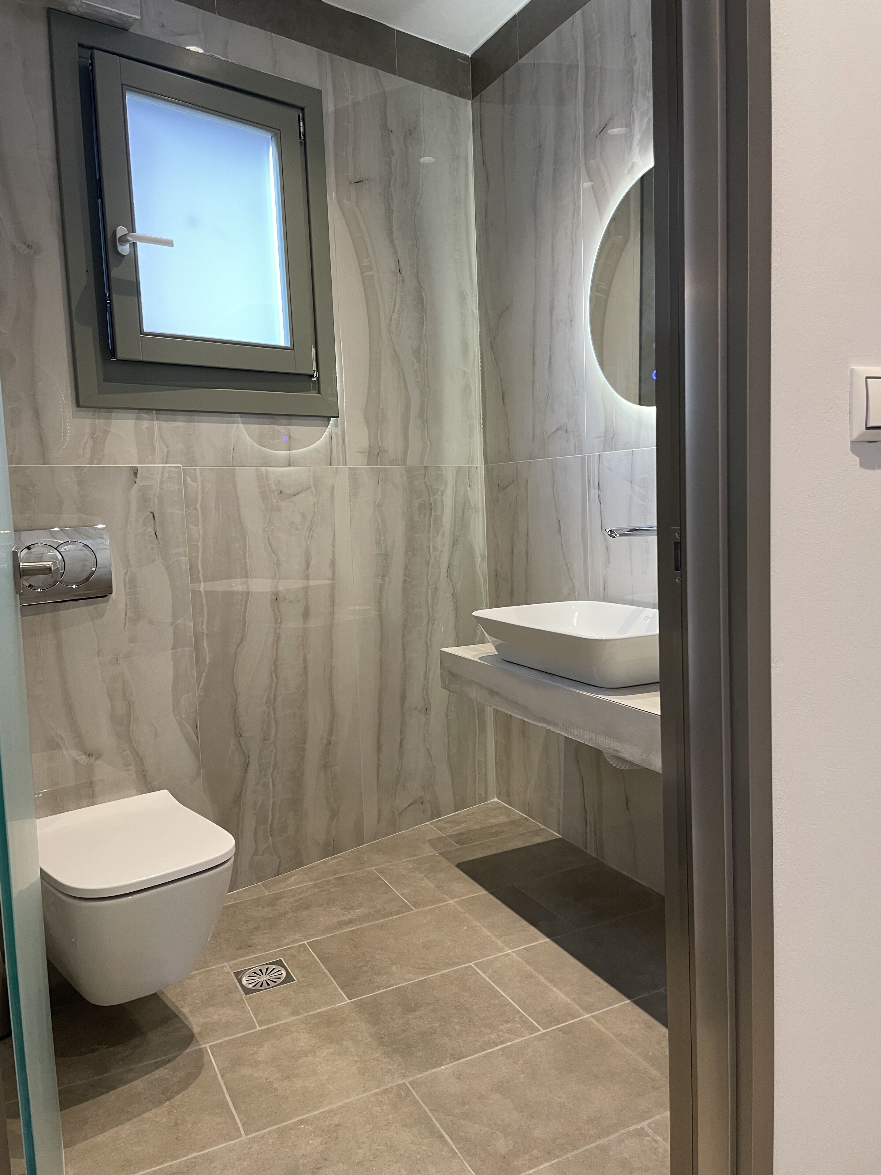Een moderne badkamer met toilet, wastafel en spiegel.