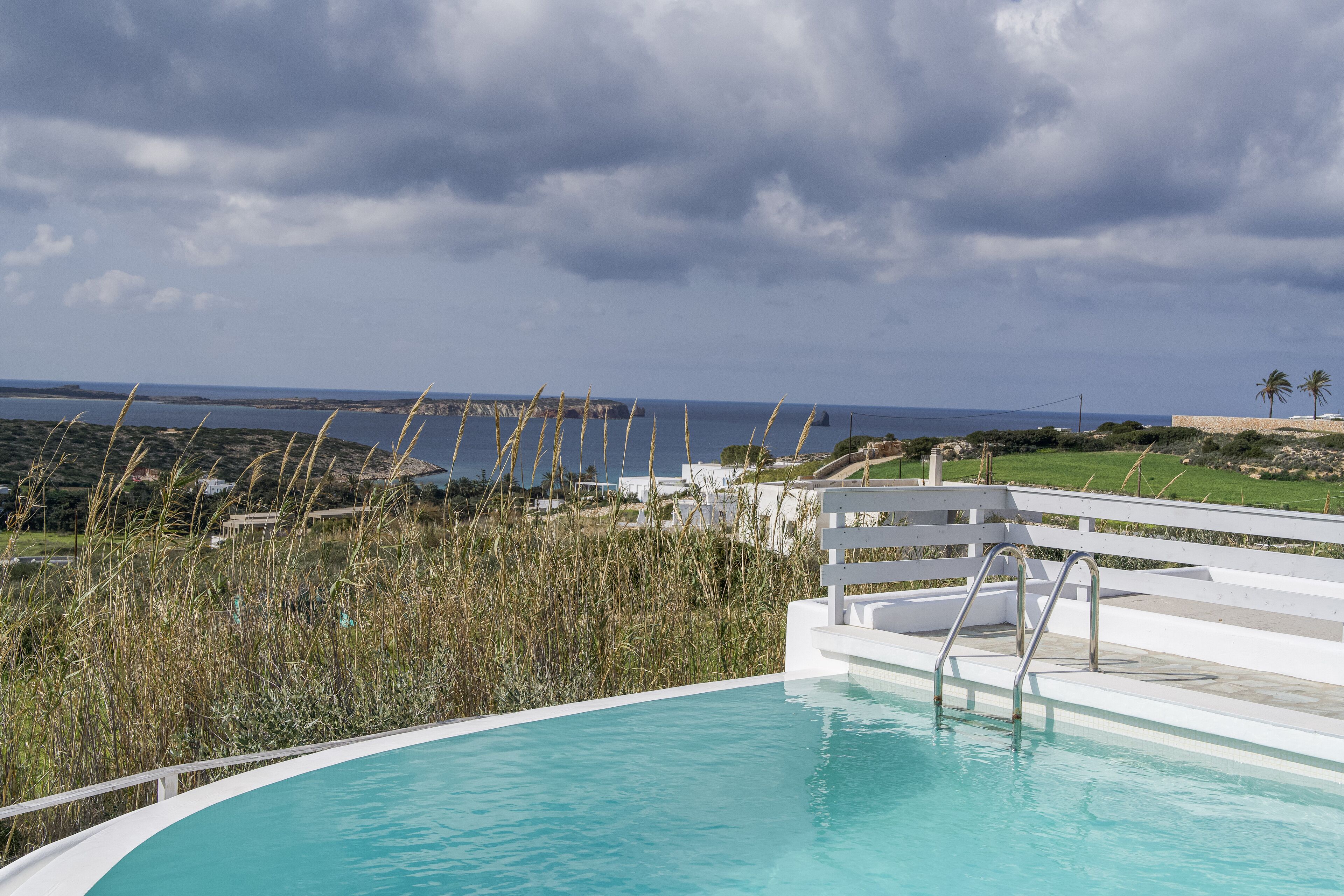 A swimming pool with a view of the sea and distant land under a cloudy sky.