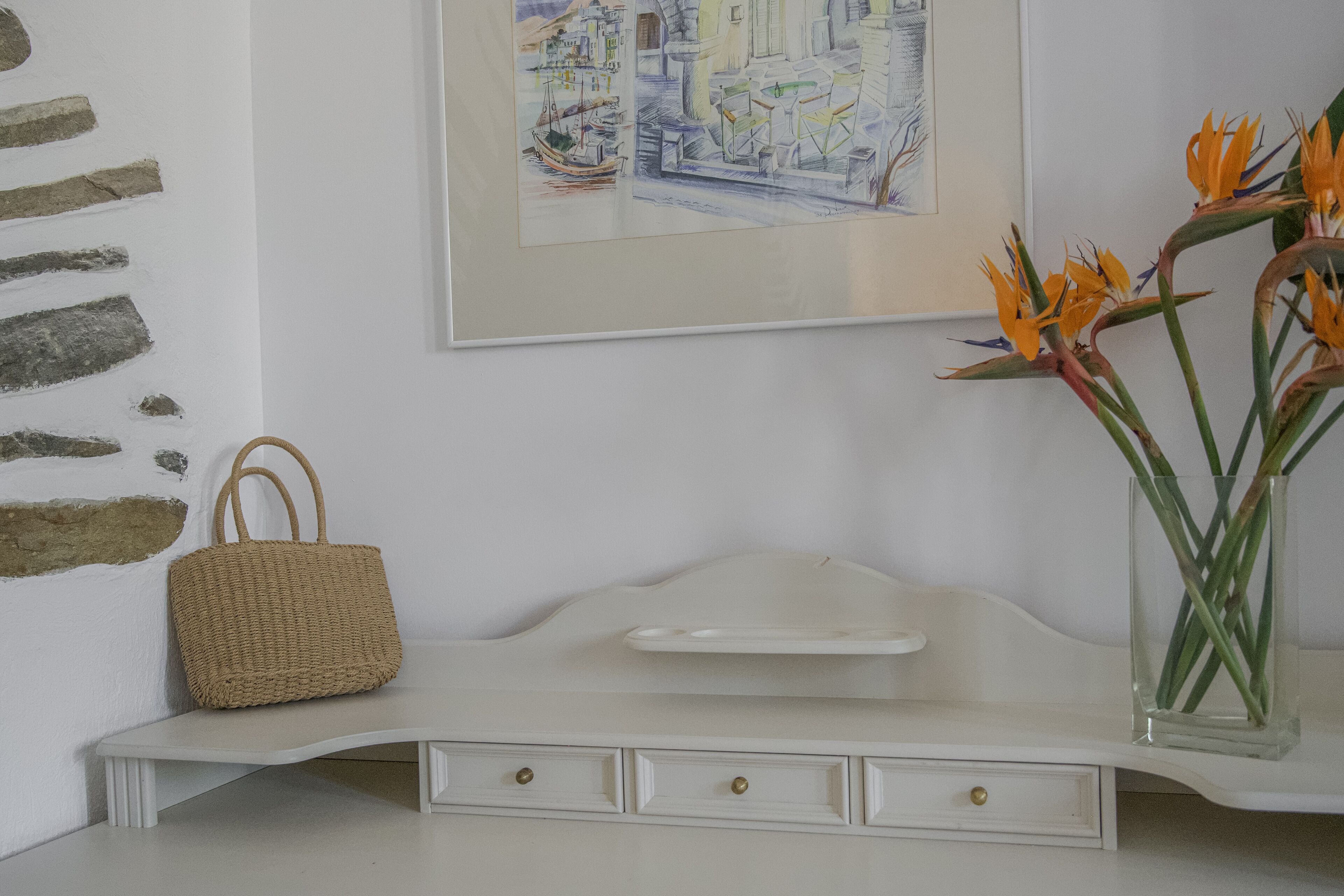 Um aparador branco com uma cesta trançada e um vaso de flores.