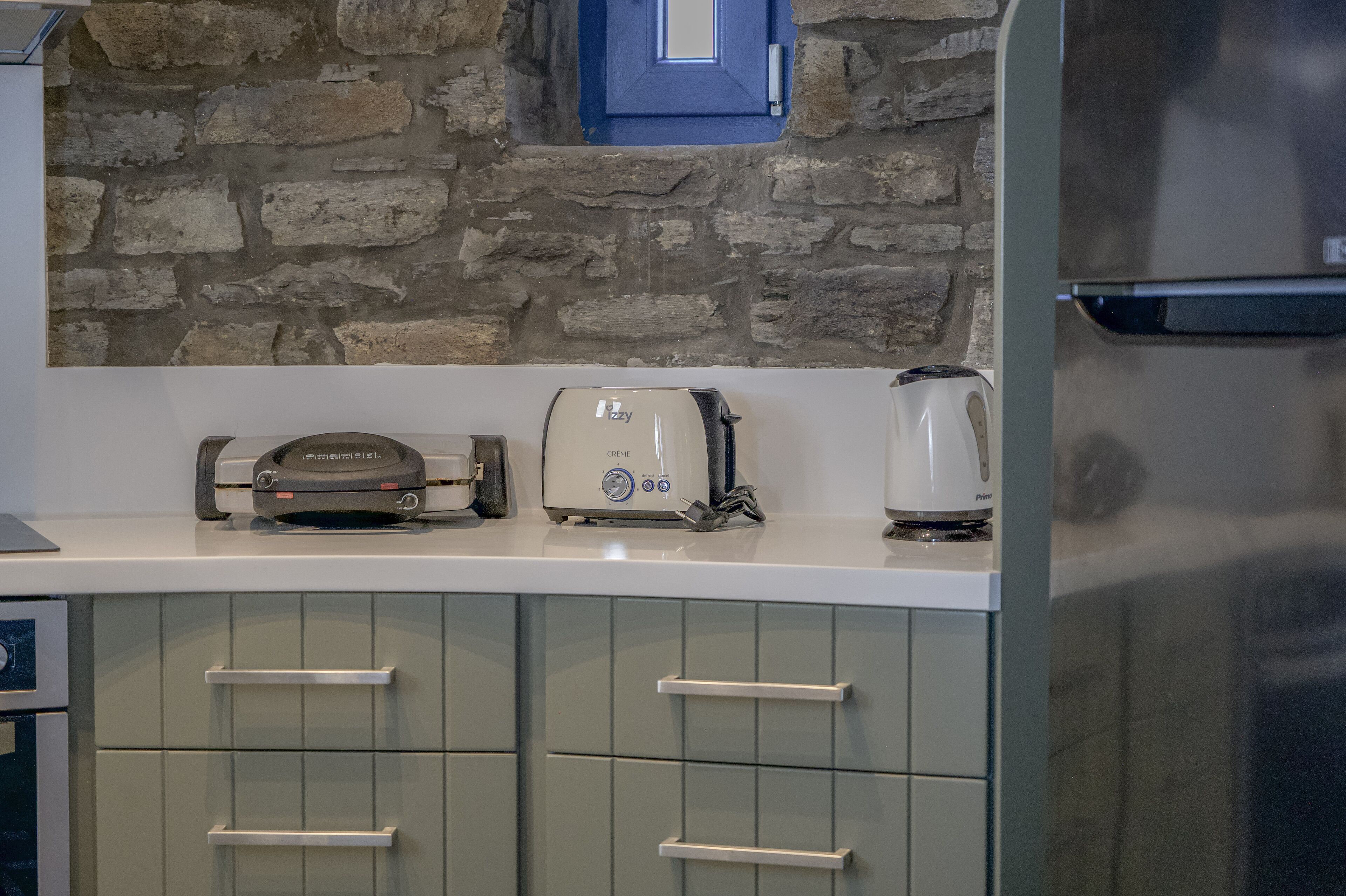 A kitchen with a stone wall, a toaster, a coffee maker, and a refrigerator.