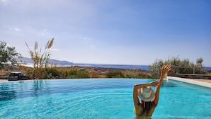 A person in a swimming pool with a view of the sea and mountains in the background. - Anthemion Paros Villas & Suites (Paros)